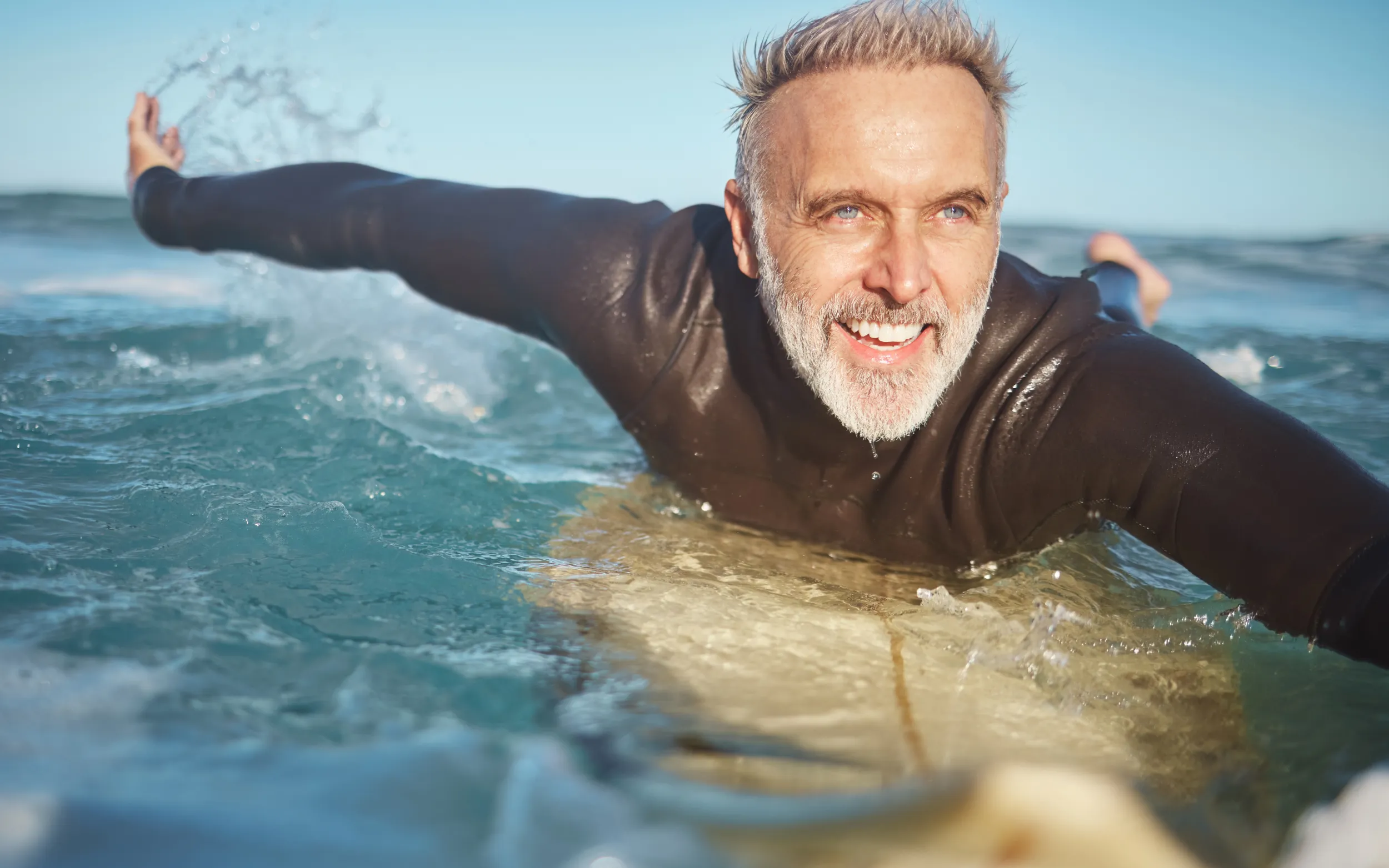 Smiling older man paddling out on a surfboard in the ocean