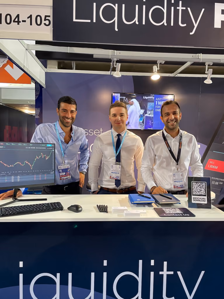 Three Match-Prime team members at the company’s expo stand with trading screens