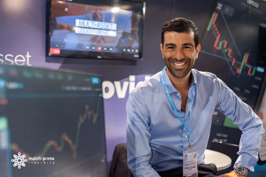 Match-Prime team member at the company’s expo stand, trading charts on the screens behind