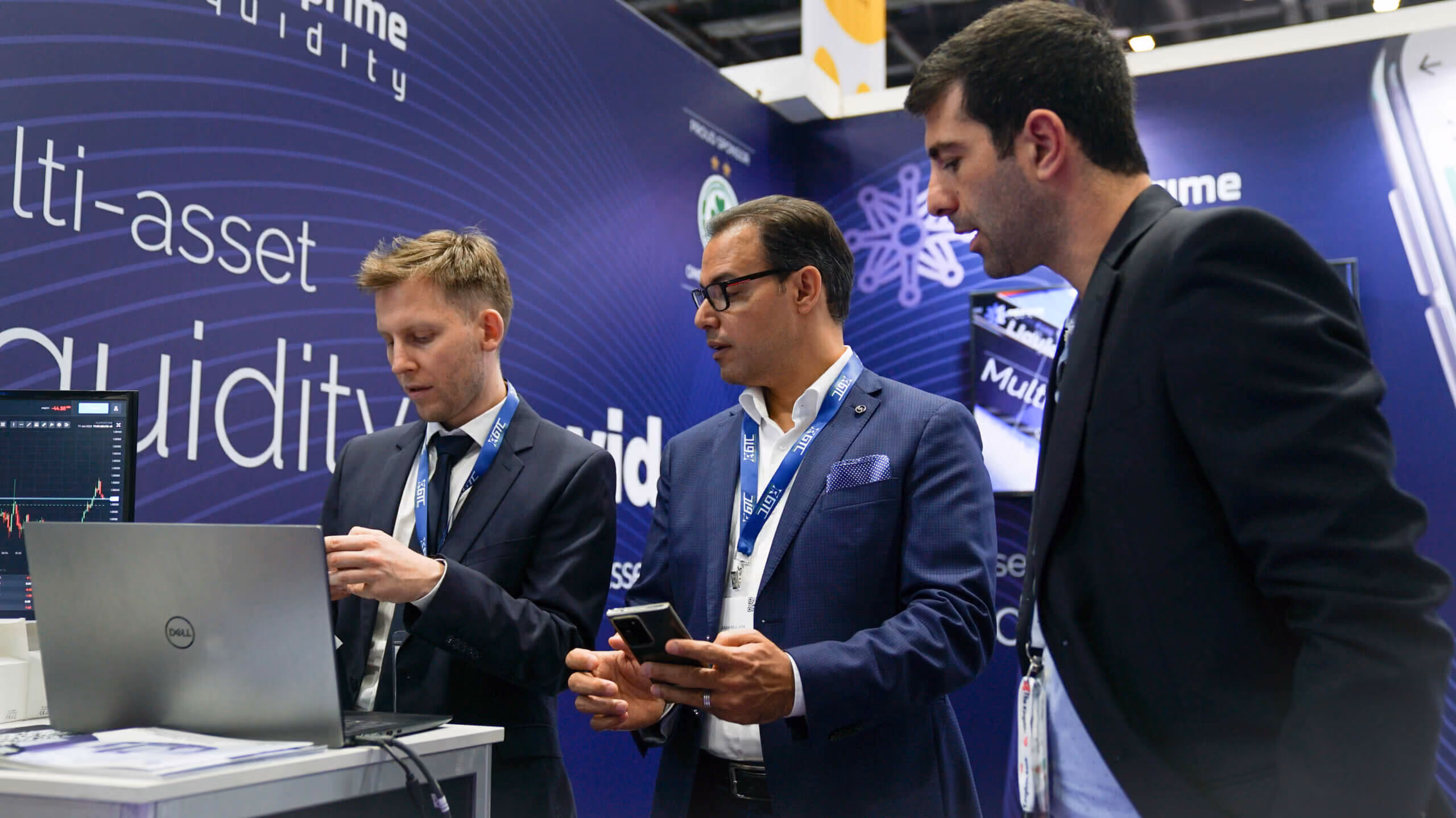 Three men reviewing a laptop together at the Match-Prime multi-asset liquidity stand.