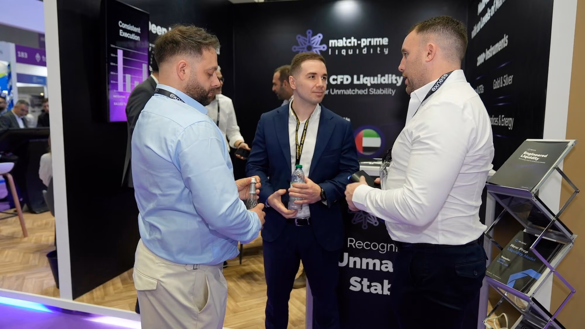 Three attendees in conversation at the Match-Prime stand, in front of a Match-Prime Liquidity Provider backdrop. 