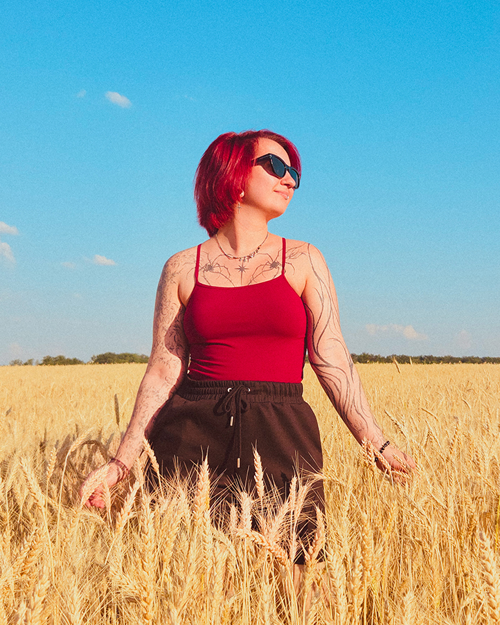 Woman with red hair and sunglasses standing in a wheat field under a blue sky