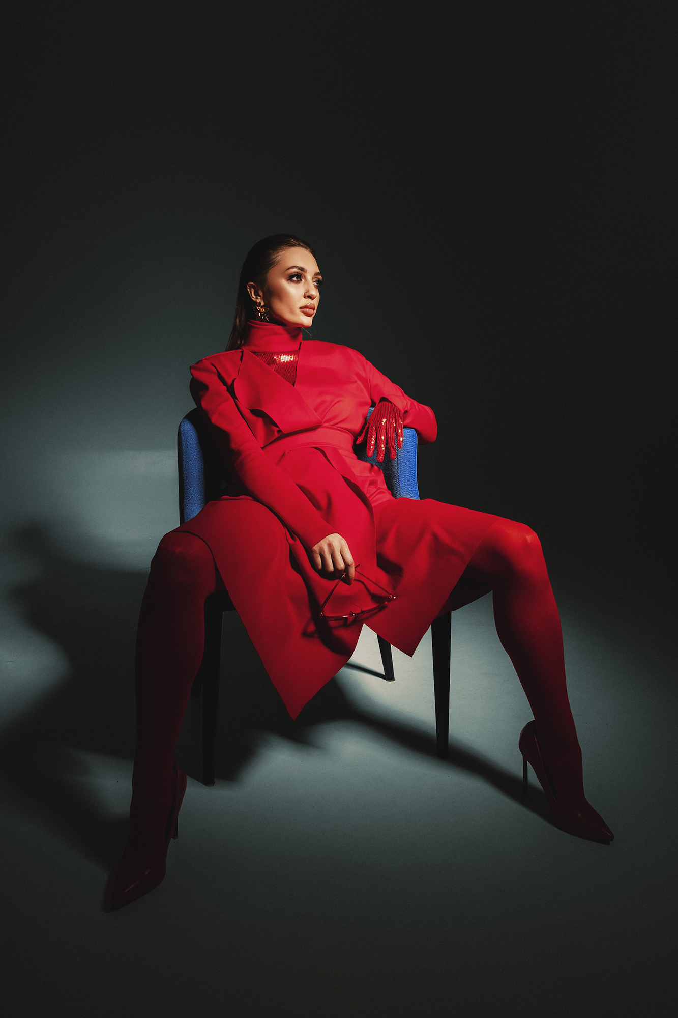 Fashion portrait of a woman in a red outfit seated against a dark background