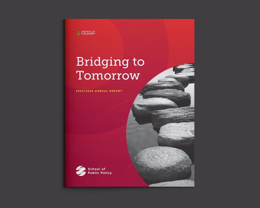 Open annual report booklet titled 'Bridging to Tomorrow 2023/2024 Annual Report' from the University of Calgary School of Public Policy, featuring a red cover design with a photo of stepping stones over water.