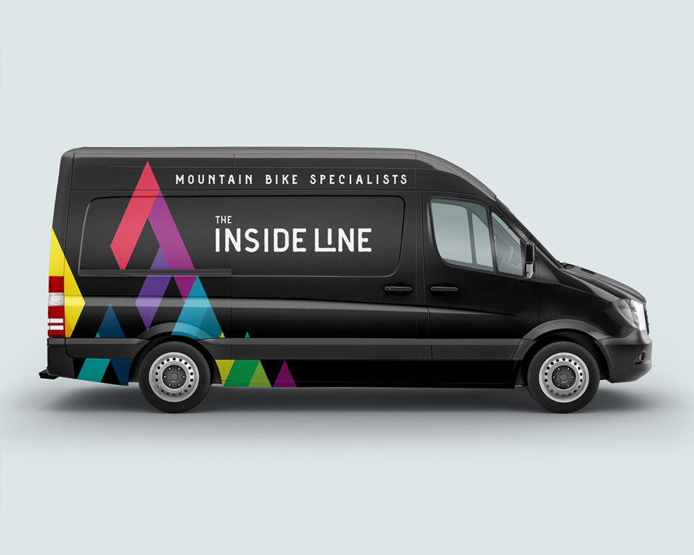 Black delivery-style van with colorful triangular mountain shapes on the side and text reading 'Mountain Bike Specialists' and 'The Inside Line'.