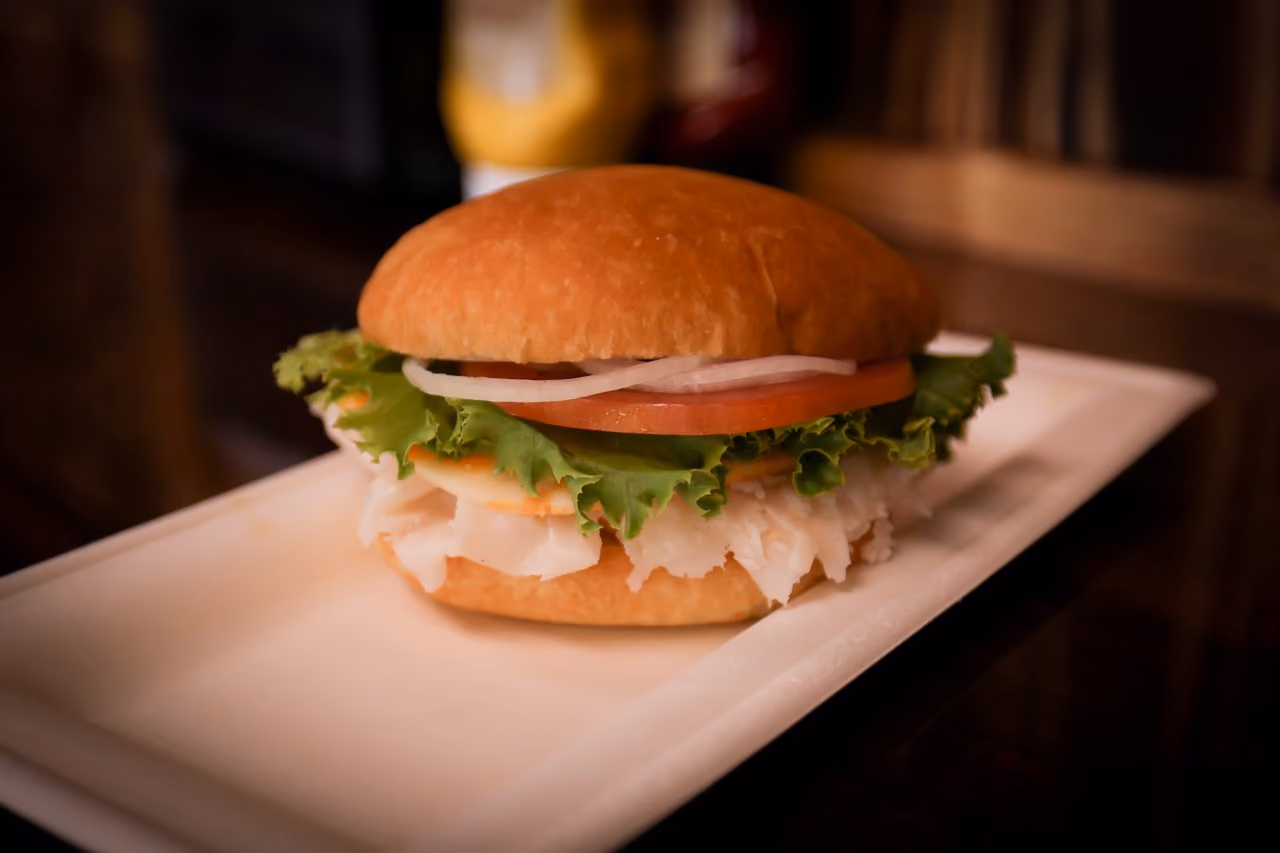 Close-up of a sandwich with lettuce, tomato, onion, and deli meat on a white rectangular plate.