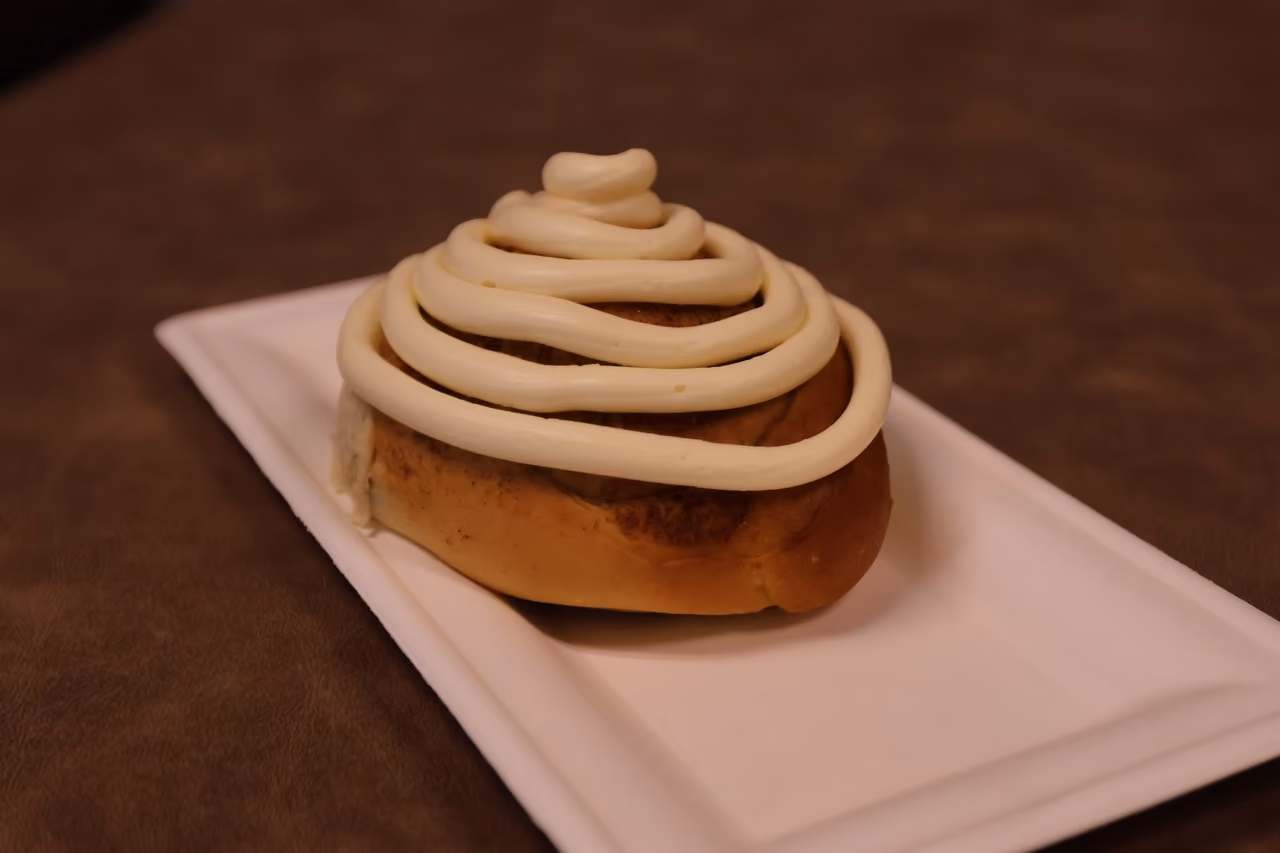 Cinnamon roll with white frosting on a rectangular white plate.