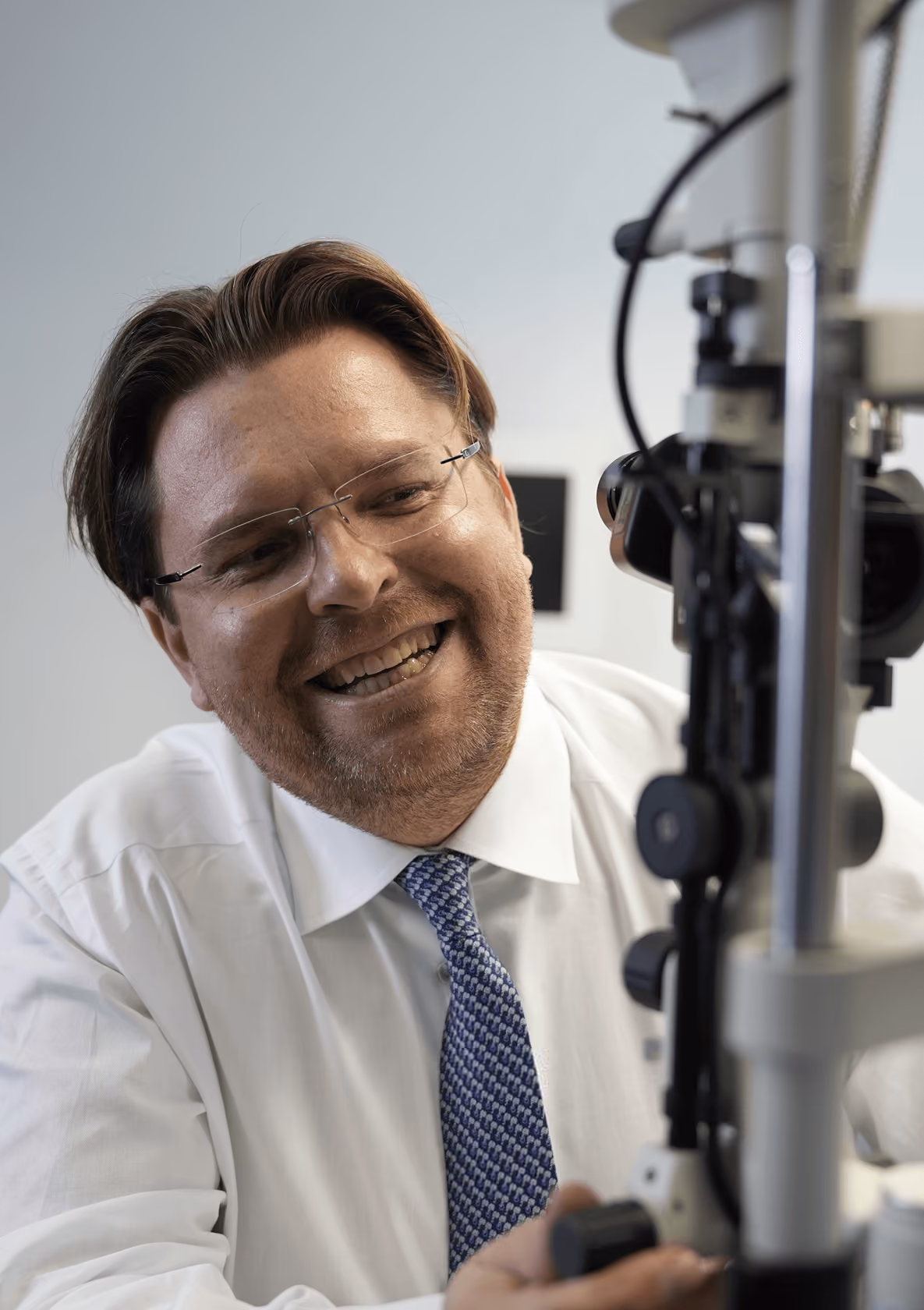 Mann mit Brille und Bart lächelt, während er Augenoptik-Gerät benutzt.