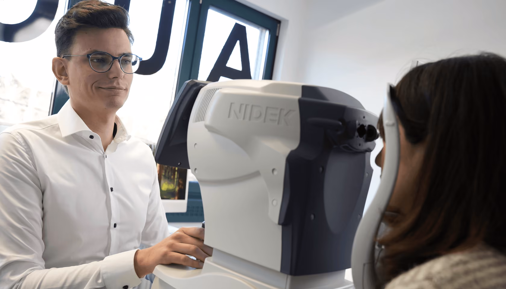 Optiker bedient modernes Augenuntersuchungsgerät; Frau sitzt gegenüber für Sehtest.
