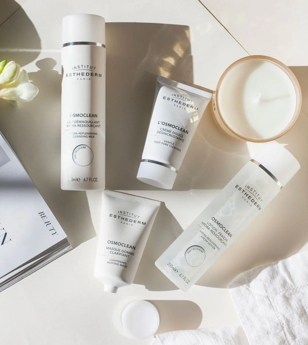 Quatre produits de soin Osmoclean Institut Esthederm sur une surface claire avec une bougie allumée.