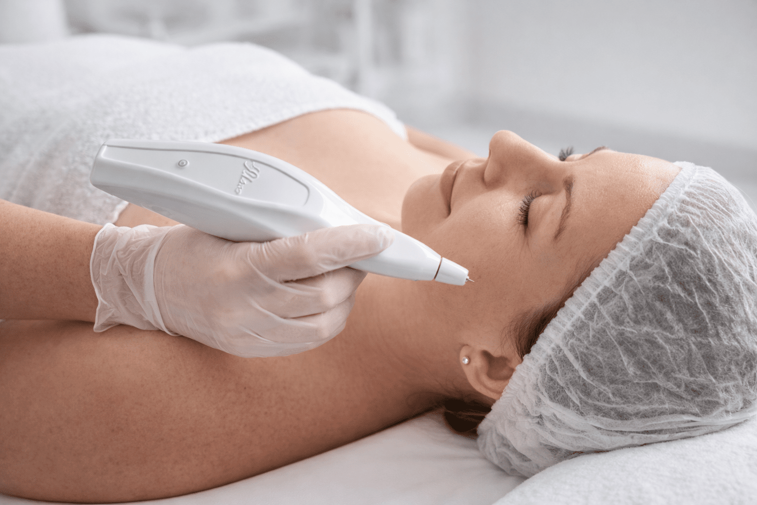 Une femme recevant un traitement de soin du visage avec un appareil esthétique en main gantée.