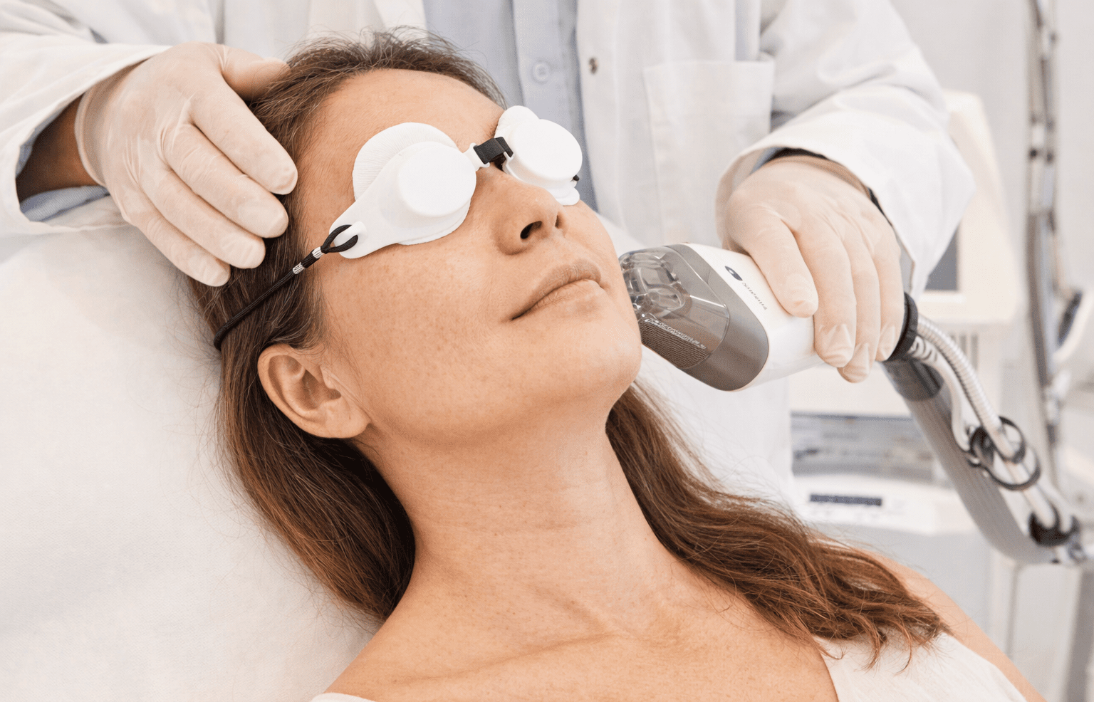 Une femme portant des lunettes de protection reçoit un traitement au visage avec un appareil laser.