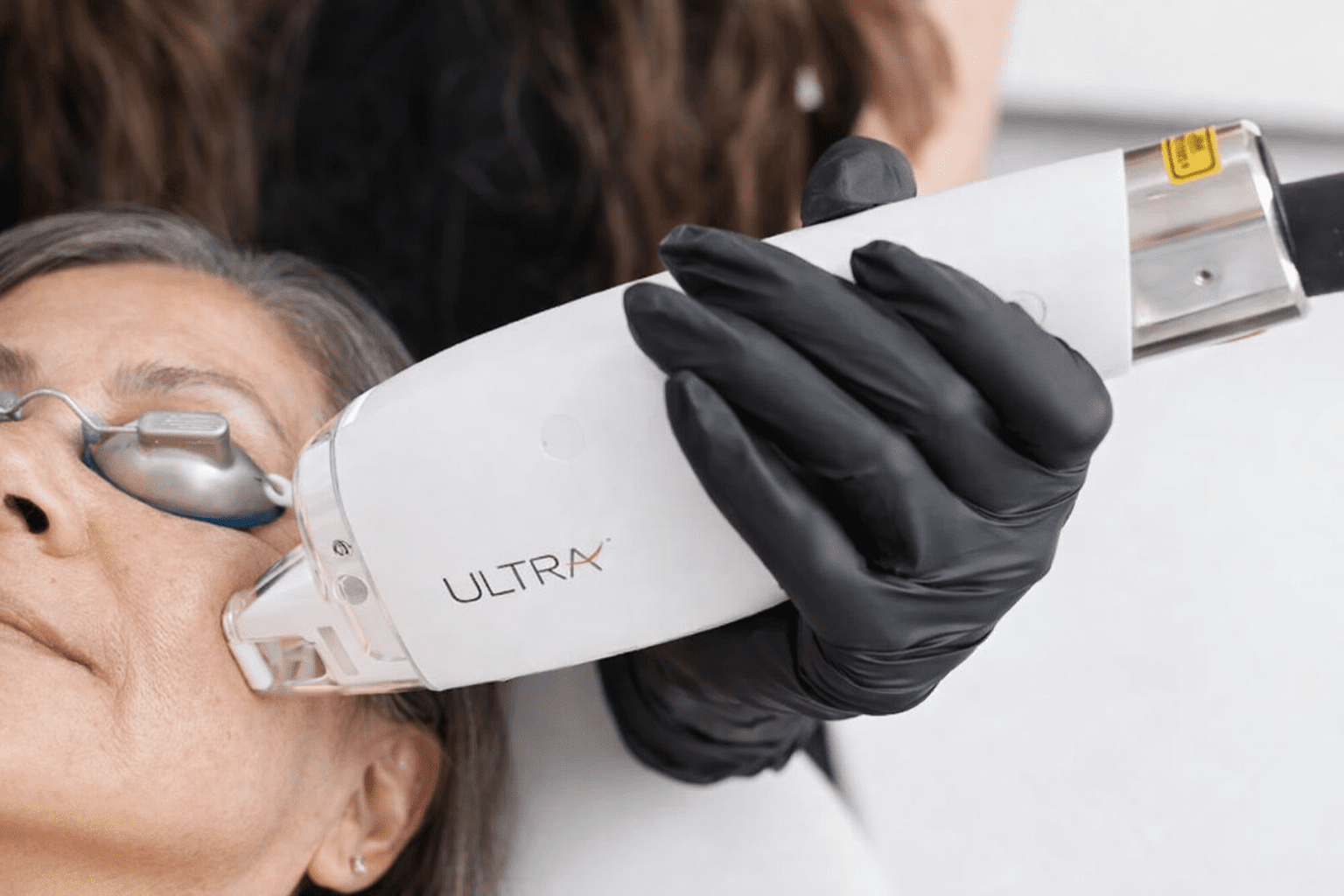 Traitement esthétique au visage avec un appareil Ultra tenu par une main gantée noire.