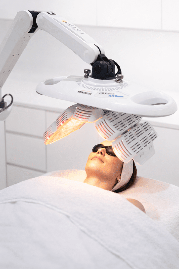 Femme portant des lunettes de protection recevant un traitement de lumière LED au visage en spa.
