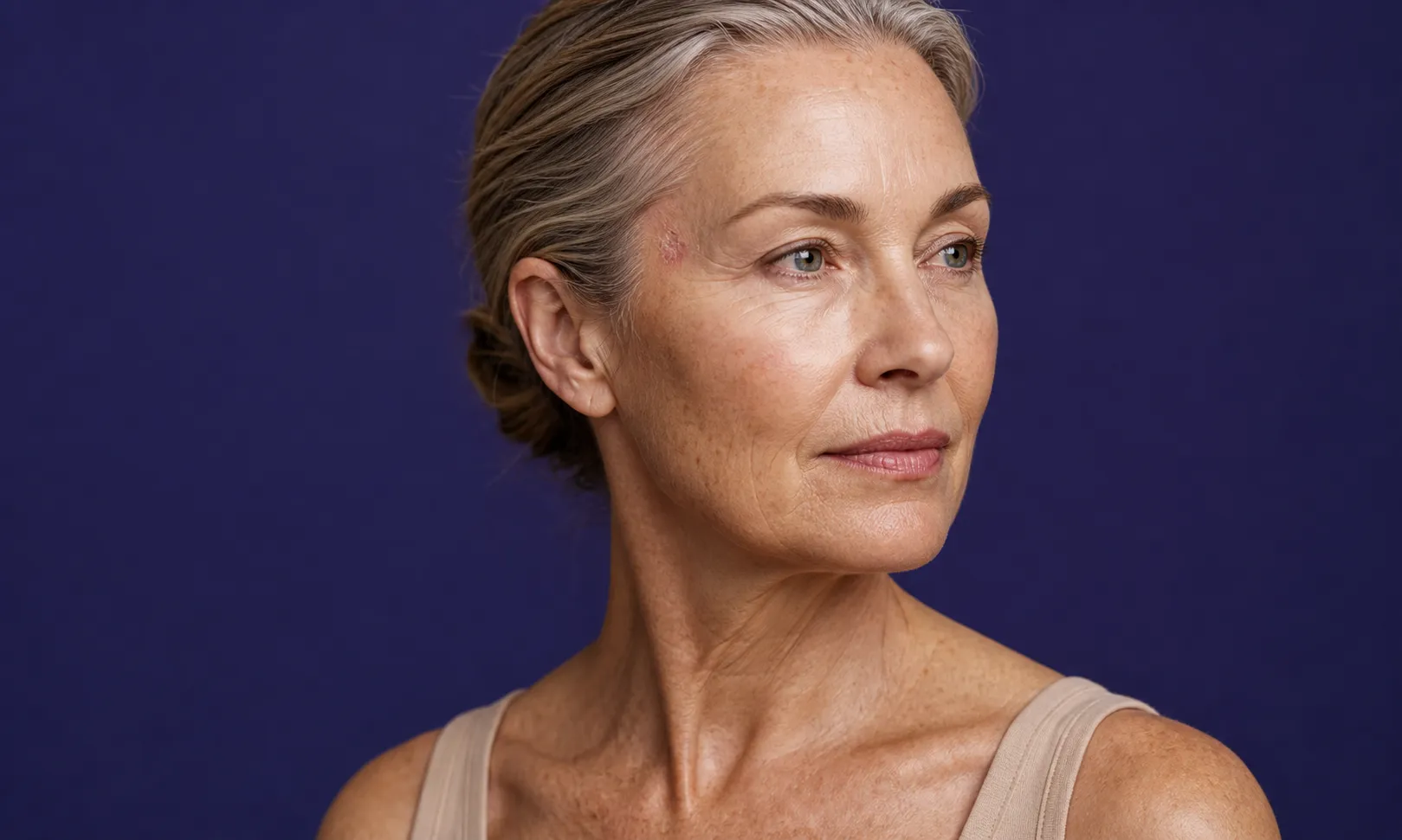 Portrait d'une femme mûre regardant sur le côté, avec une peau claire et des cheveux gris en chignon.