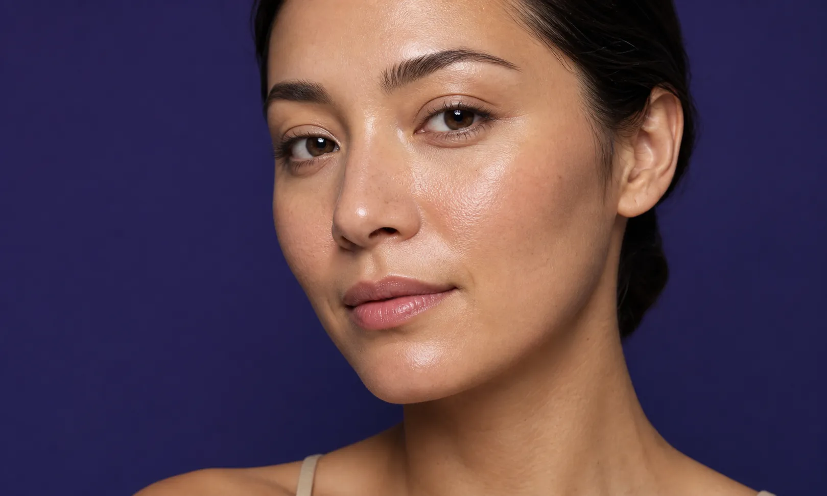 Portrait d'une femme avec une peau lisse et éclatante sur fond violet.