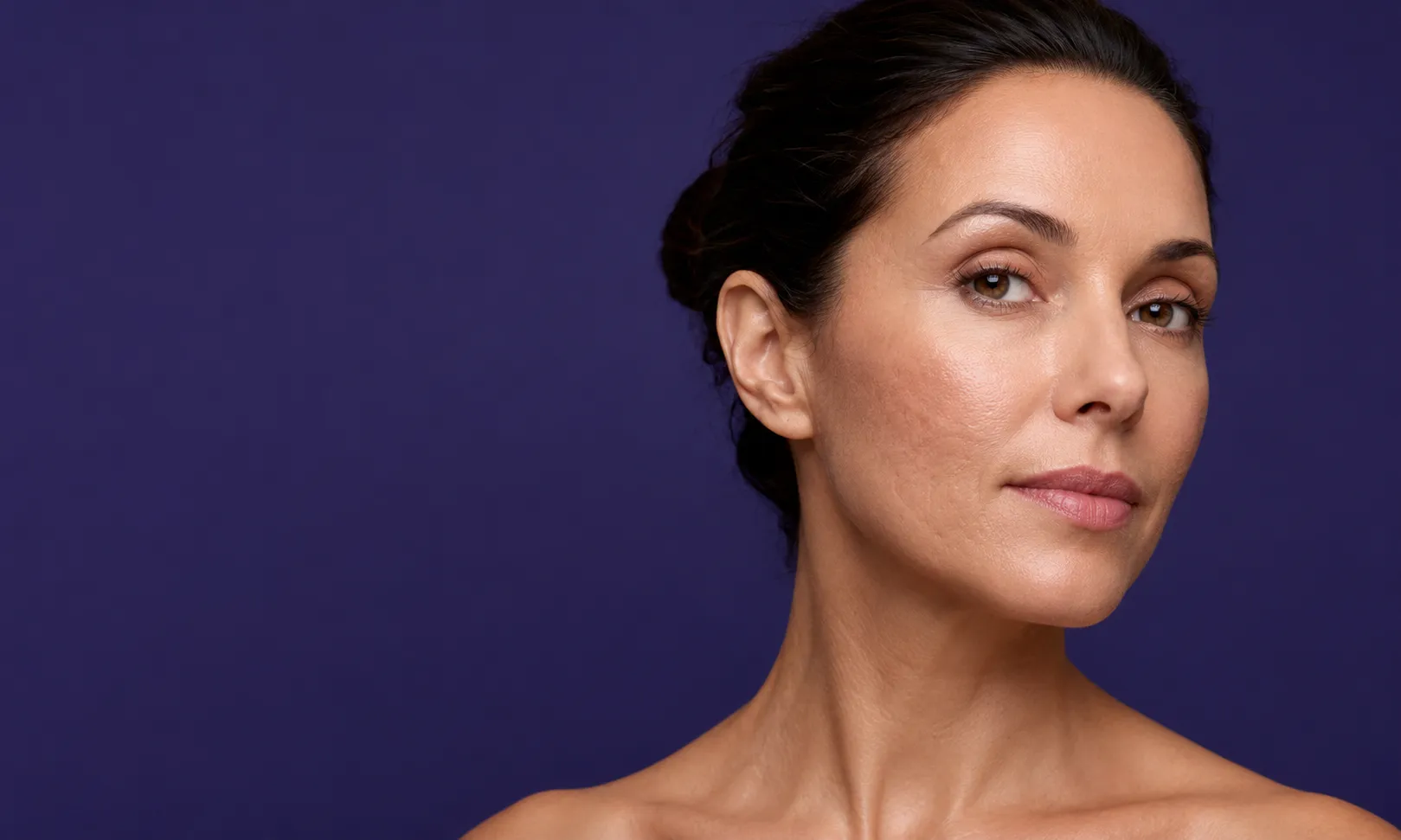 Portrait d'une femme montrant une peau claire et lisse sans cicatrices sur fond violet.