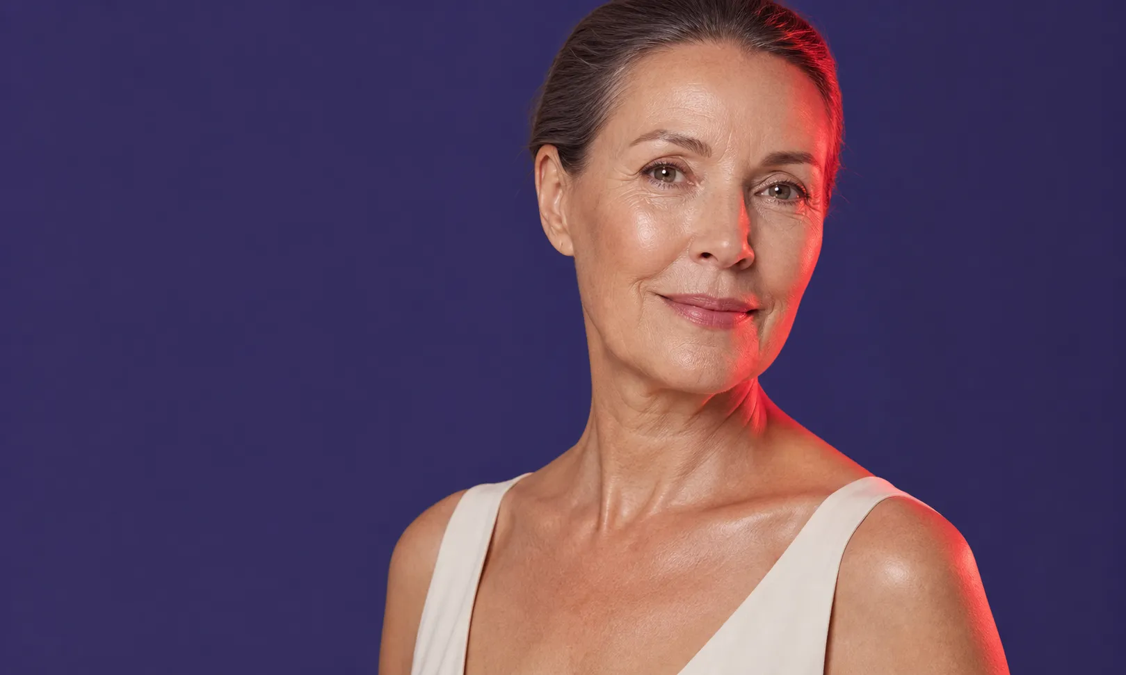 Portrait d'une femme mûre souriante, peau lumineuse, portant une robe beige sur fond violet.