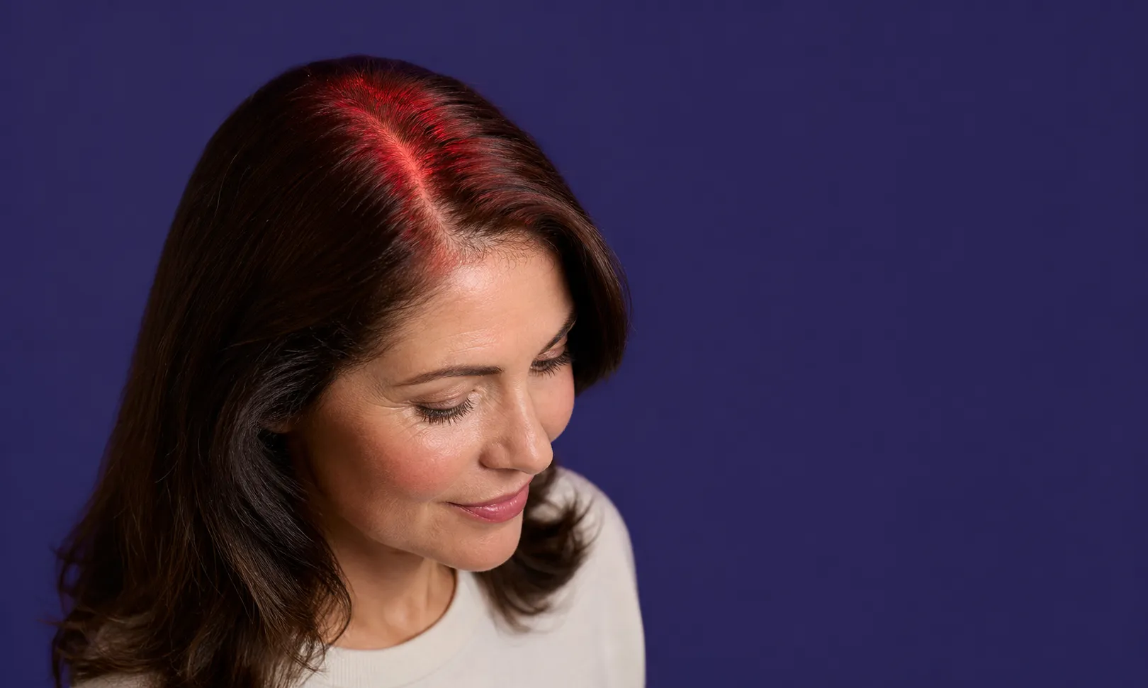 Femme avec les cheveux bruns et une lumière rouge sur le cuir chevelu, fond bleu foncé.