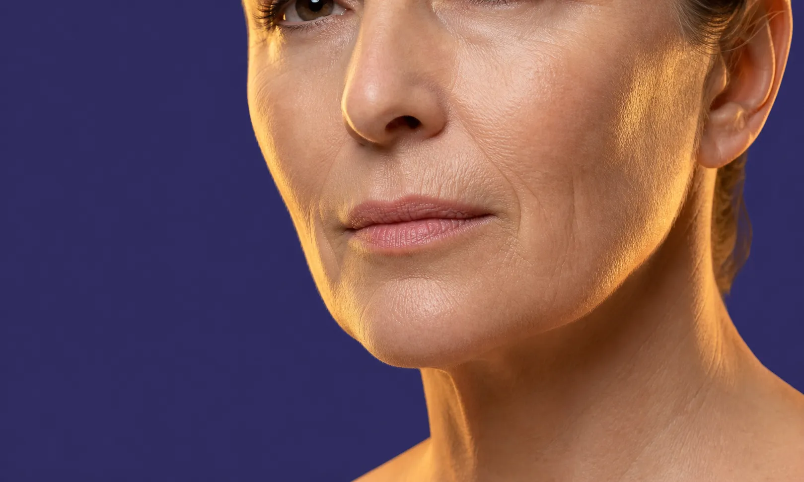 Gros plan sur le bas du visage d'une femme avec rides visibles sur peau mature, fond violet.