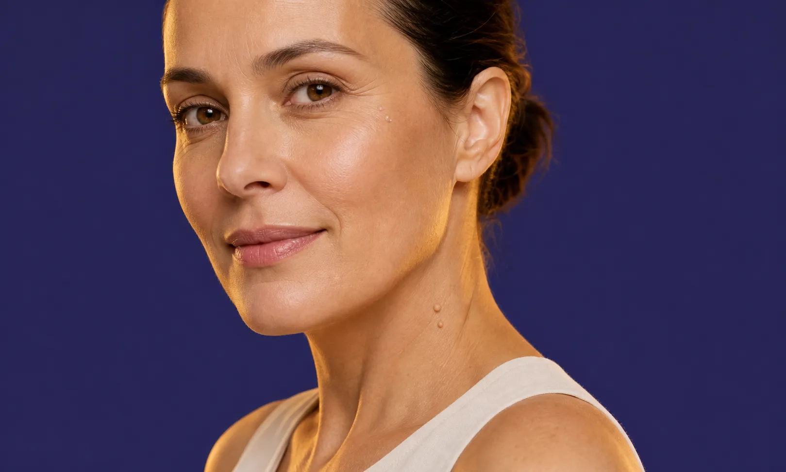 Femme souriante à la peau claire avec acrochordons visibles au cou sur un fond bleu uni.