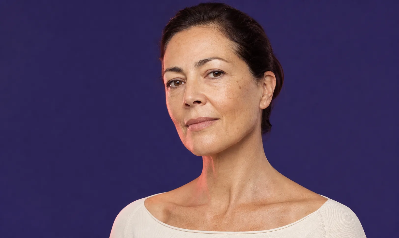 Portrait d'une femme d'âge moyen avec un haut blanc et un fond violet.