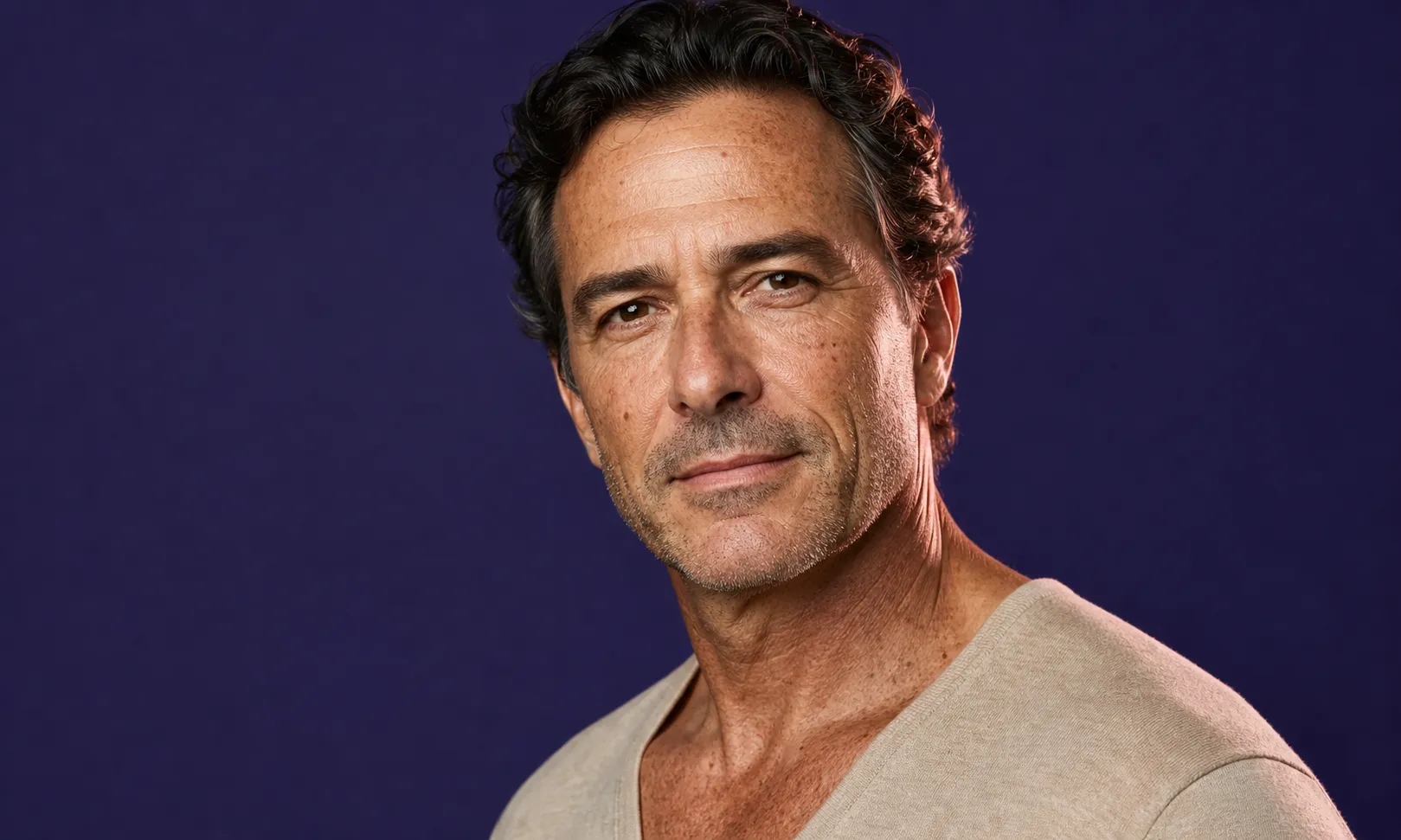 Portrait d'un homme d'âge moyen avec cheveux bouclés et teint bronzé, fond violet.