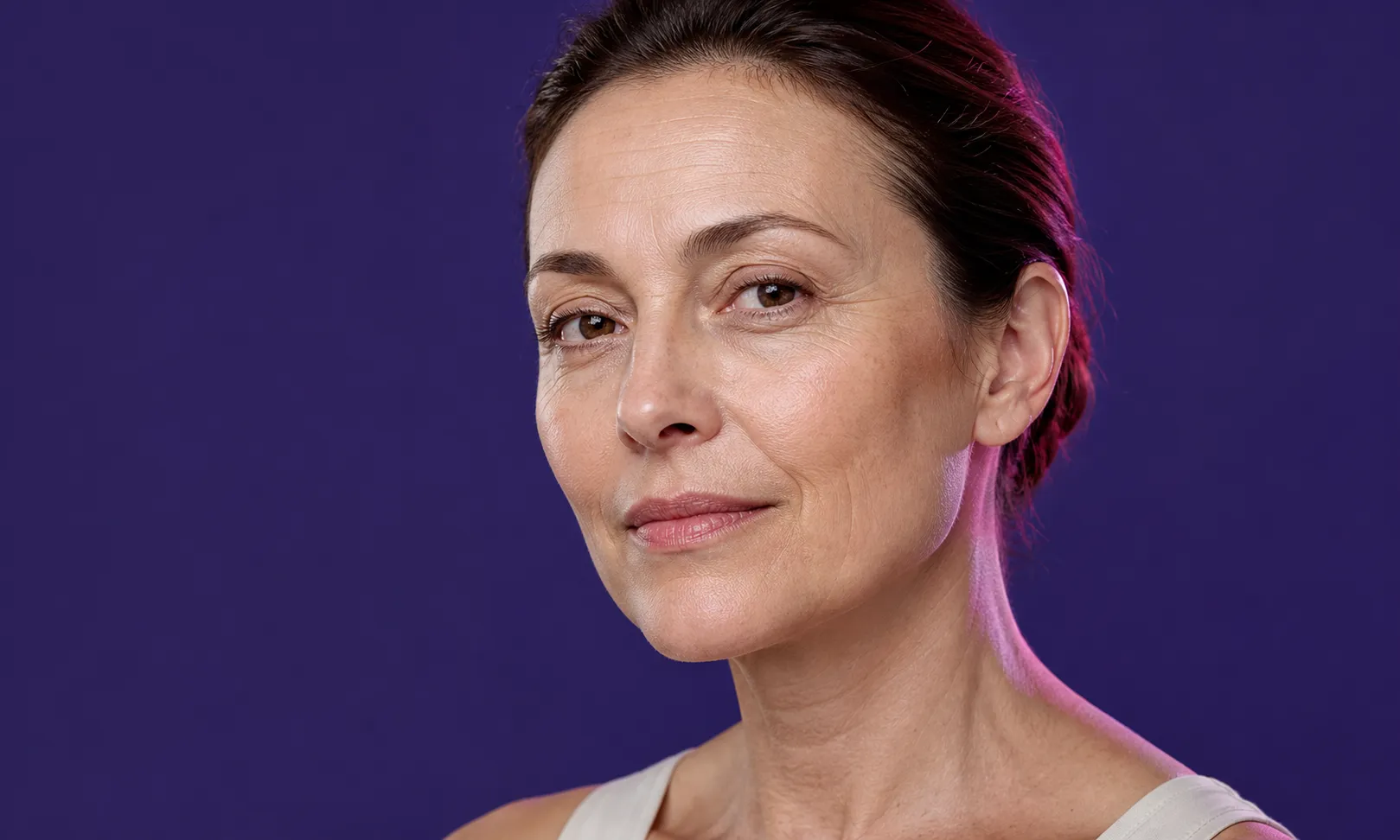 Portrait d'une femme d'âge moyen avec cheveux bruns tirés en arrière sur fond violet.