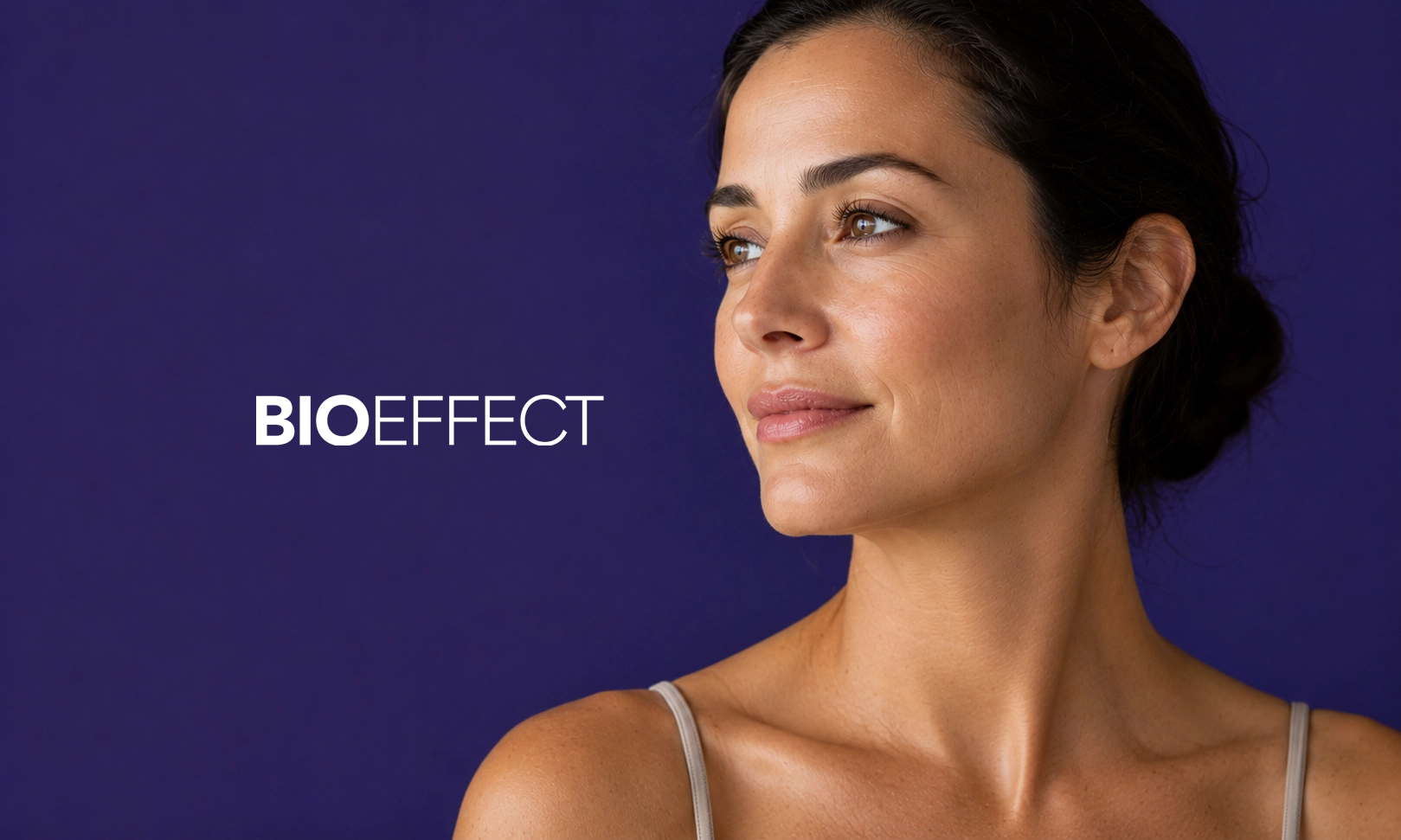 Portrait d'une femme souriante avec une peau éclatante, regardant vers la droite, sur fond violet avec le texte BIOEFFECT à gauche.