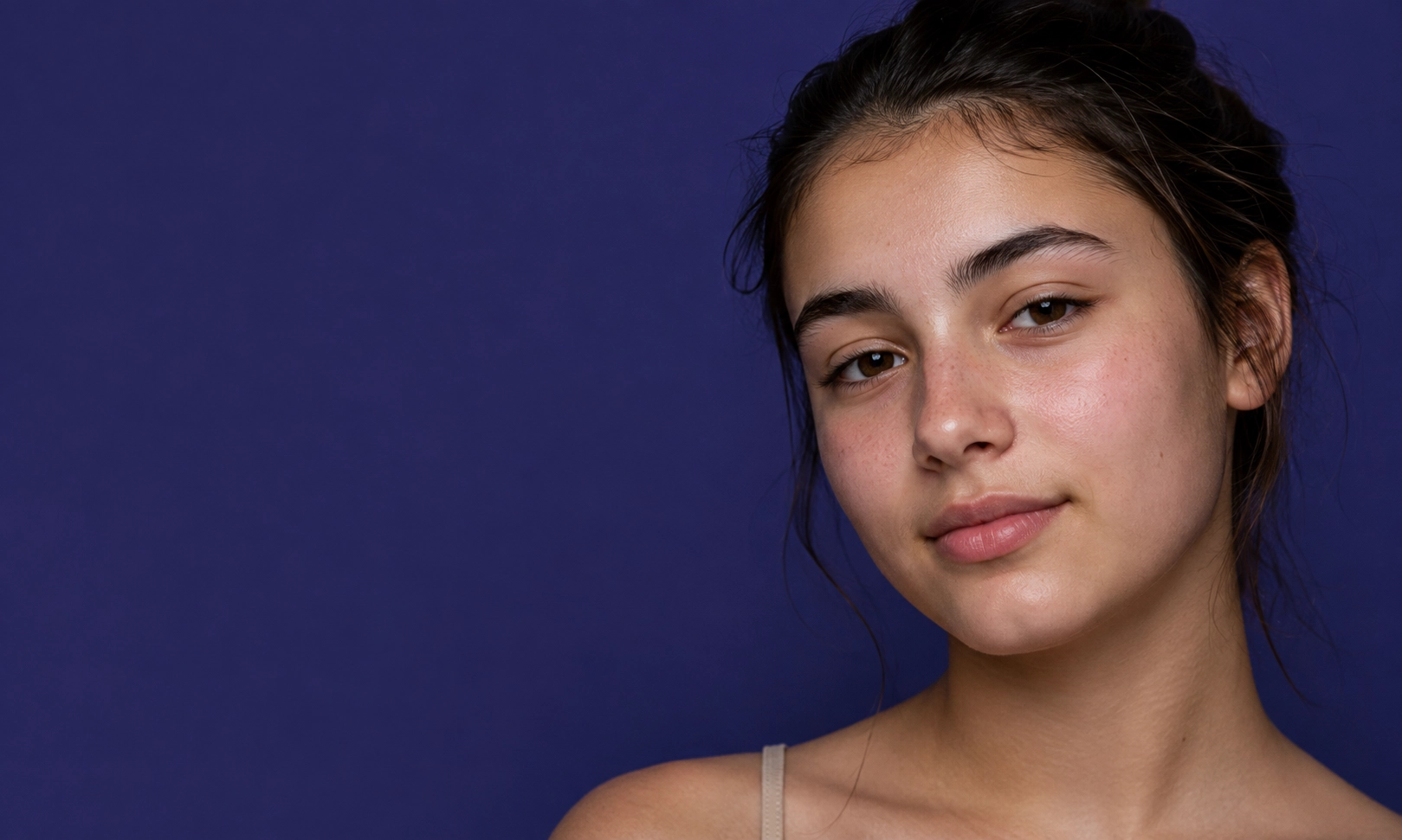 Portrait d'une adolescente souriante avec des cheveux bruns attachés, portant un haut à fines bretelles, sur un fond uni violet.