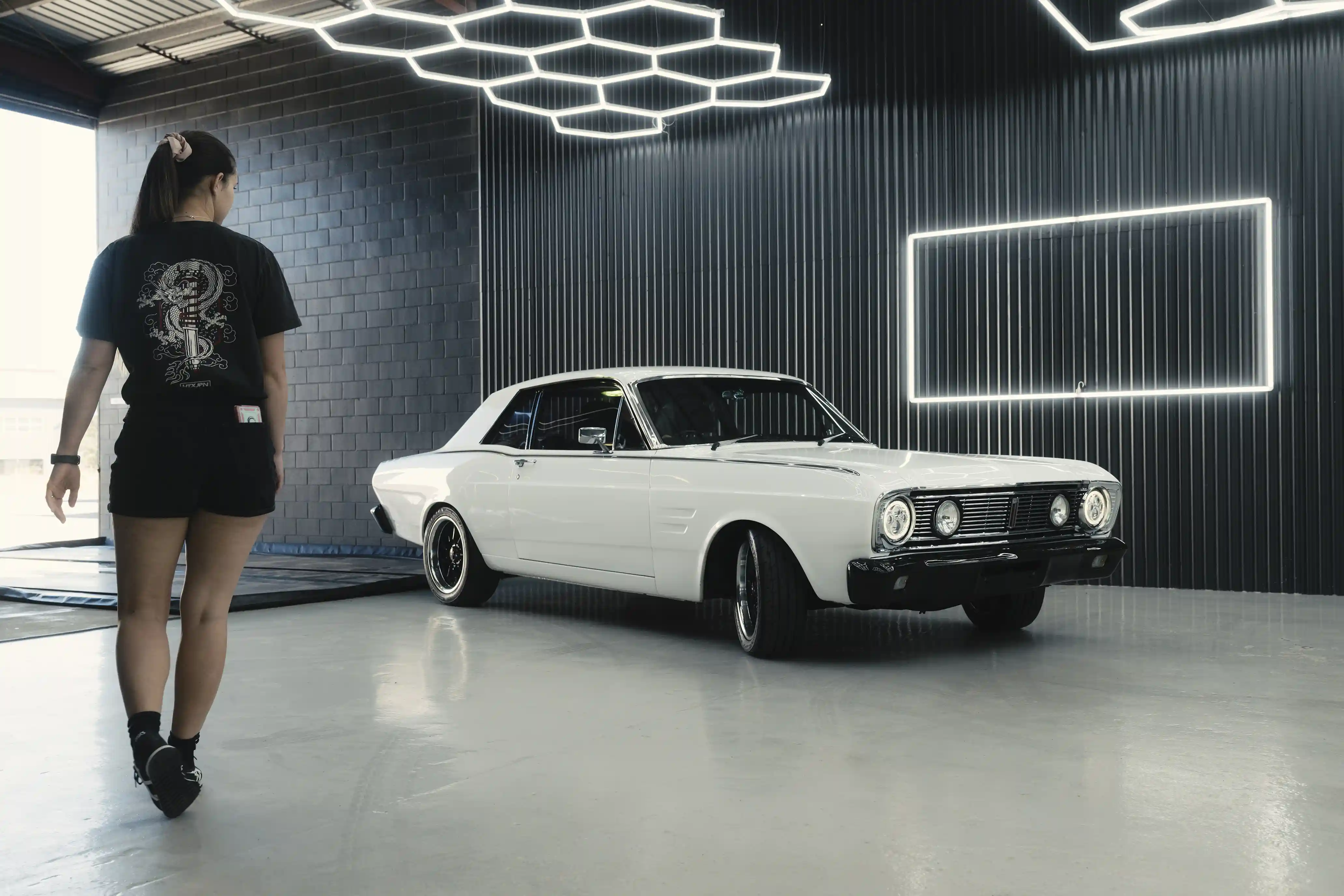 Owner of Ghostline, Layni, walking towards a white Ford Falcon in the workshop.