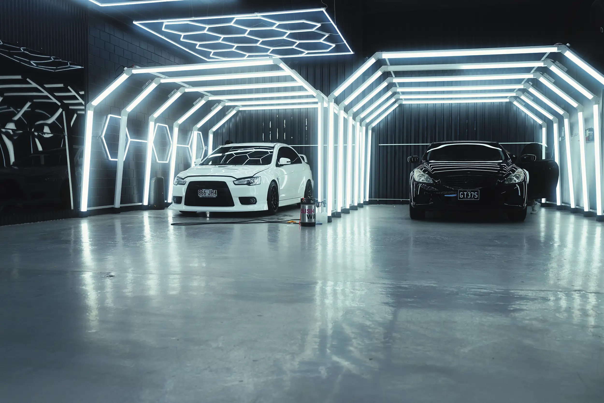 Two cars parked under paint inspection lights.