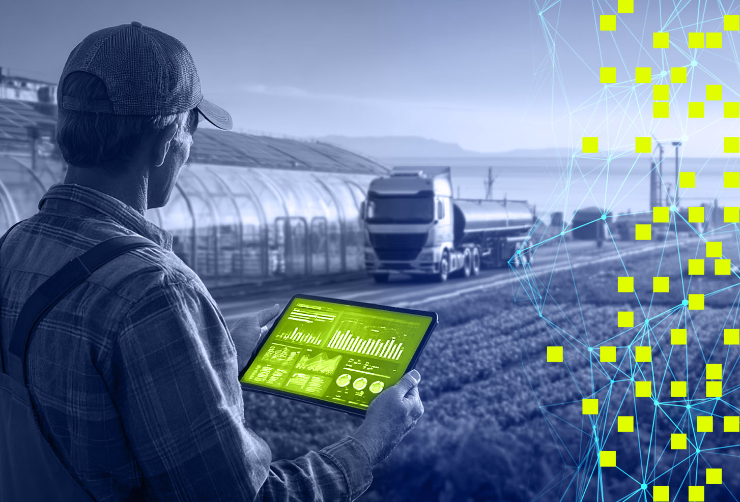 Farmer holding tablet with data charts in front of greenhouse and tanker truck on farm road.