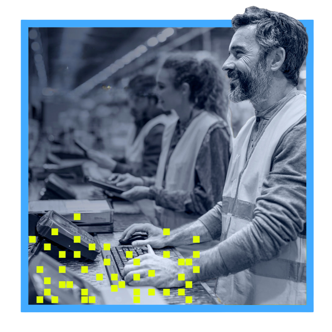 Smiling male factory worker typing on keyboard with two colleagues using tablets in background.