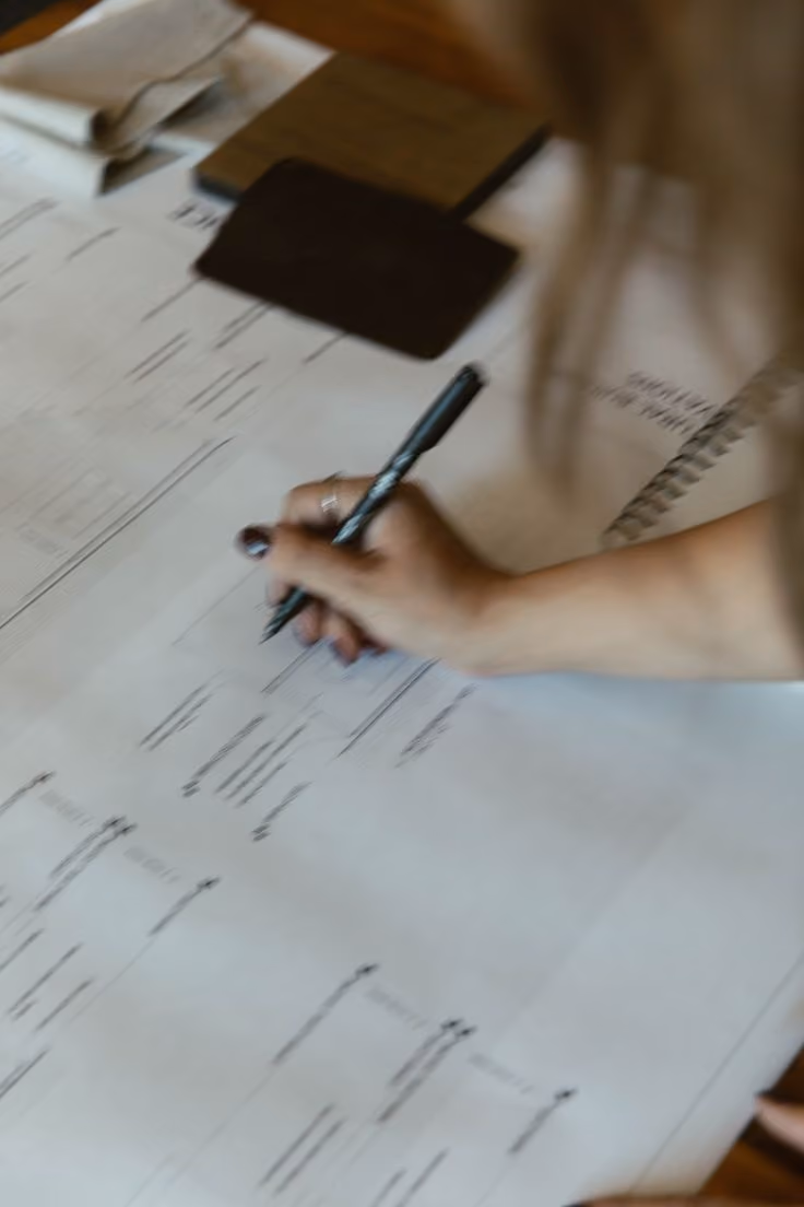 Hand holding pen writing or drawing on large paper with notes and flowcharts.
