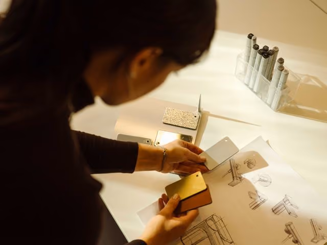 Person holding phone cases above sketches and design prototypes on a table.