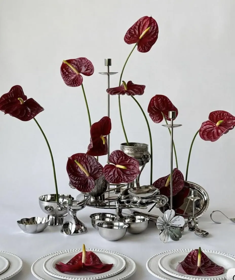 Table centerpiece with red anthurium flowers in silver bowls and three anthuriums on white plates.