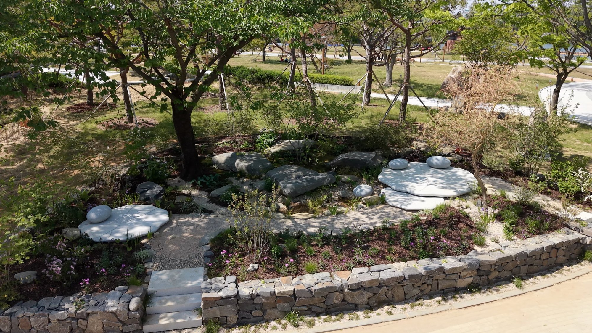 돌담 안쪽으로 식생대와 연잎 오브제, 너럭바위가 놓인 정원 「수릿날, 연잎에 스미다」