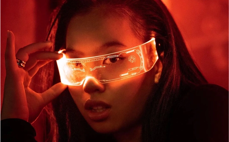 Woman wearing glowing futuristic visor glasses with digital HUD graphics in a red-lit setting.