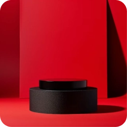 Two black cylindrical pedestals stacked on a bright red background casting shadows.