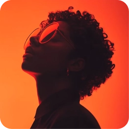 Profile of a person with curly hair wearing sunglasses against an orange-red background.