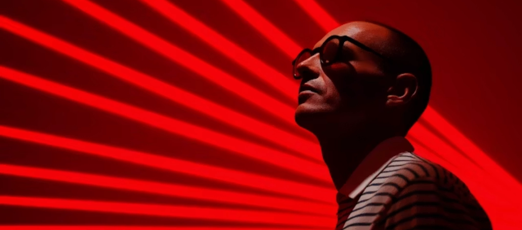 Man wearing sunglasses and striped shirt looking up against a red background with radiant red stripes.