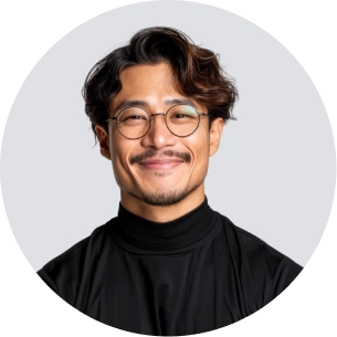 Smiling man with glasses, mustache, and wavy hair wearing a black turtleneck against a light background.
