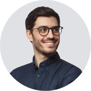 Smiling man with glasses and short dark hair wearing a dark button-up shirt against a gray background.