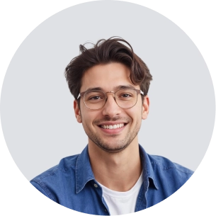 Smiling young man with glasses, dark hair, wearing a blue shirt and white t-shirt in front of a gray background.