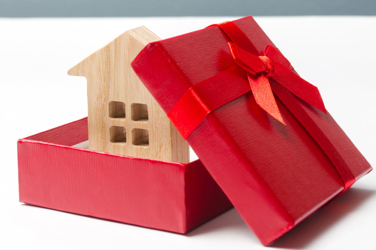 Small wooden house figurine inside an open red gift box with a matching red ribboned lid leaning against it.