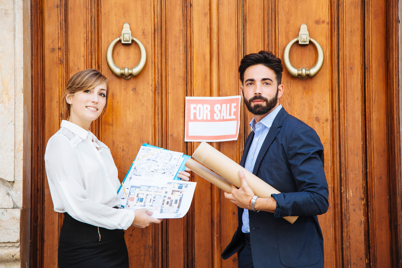 A woman and a man standing in front of large wooden doors with a 'For Sale' sign; the woman holds architectural plans and the man holds rolled-up blueprints, suggesting a property sale or real estate context.