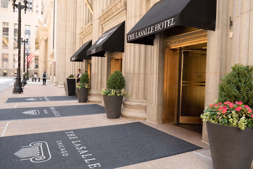 Entrance of The LaSalle Hotel in Chicago with black awnings, potted plants, and doormats with hotel logo.