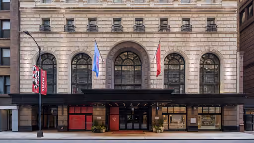 Historic stone building facade with arched windows and flags outside a black awning entrance.