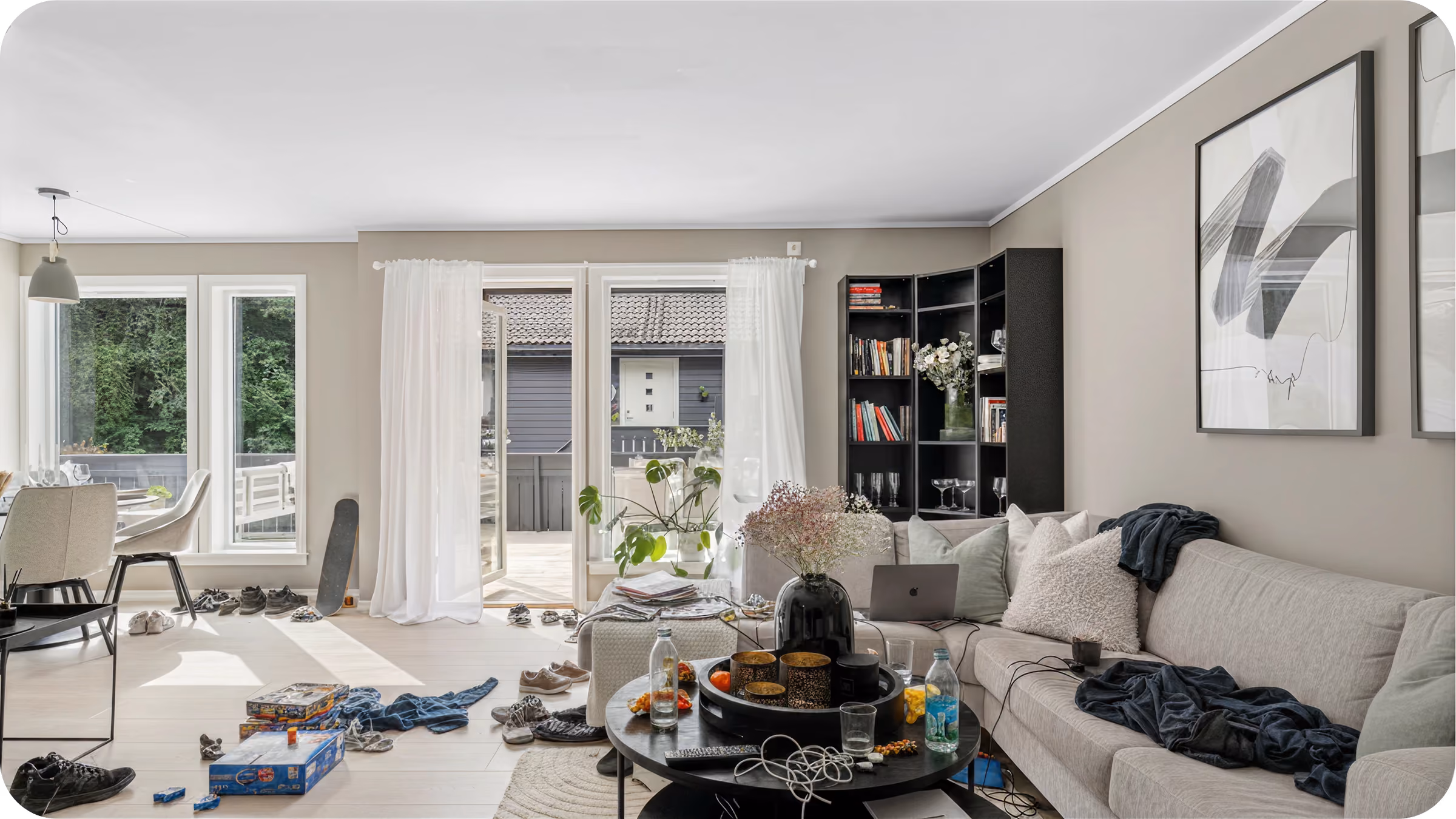 Living room with beige sofa, black round table cluttered with items, and an open door to a patio.